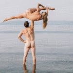 Rear view of nude man lifting nude woman doing the splits